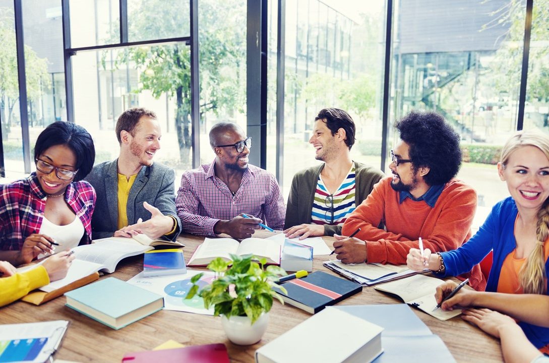 A diverse group of people discussing around a table with books and notebooks.